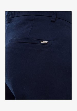 Tumed sinine kangast püksid, millel on sile tekstuur, tagaküljel on tasku metallmärgiga, millel on kirjas "BIG STAR". Lihtne, kohandatud disain.