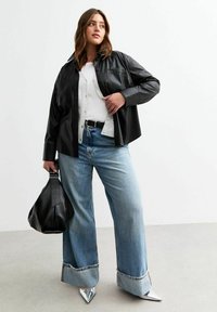 Zwart leren button-up shirt over een grijze cardigan, gecombineerd met lichtblauwe wijde jeans. Afgewerkt met zilveren puntige hakken en een zwarte tas.
