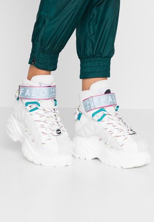 Valkoiset tikatut korolliset tennarit paksuilla pohjilla, monivärisillä nauhoilla, sinivihreillä yksityiskohdilla ja vaaleansinisisillä remmeillä, joita yhdistetään vihreisiin käännettyihin housuihin.