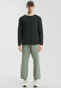 Pull en maille noir texturé, T-shirt gris clair en dessous, pantalon vert sauge avec cordon de serrage et baskets blanches avec accents noirs.