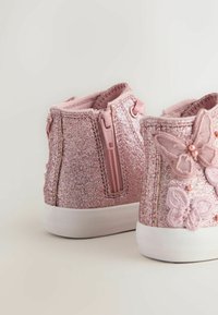 Różowe, błyszczące sneakersy typu high-top mają zamek błyskawiczny, wyściółkę z materiału oraz haftowane akcenty w kształcie motyla z perłowymi detalami po bokach.