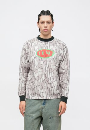 Pikad varrukadega dressipluus tekstuurse halli mustriga, musta kraega ning keskel punase ja rohelise logoga. Komplektses roheliste cargo-pükstega.