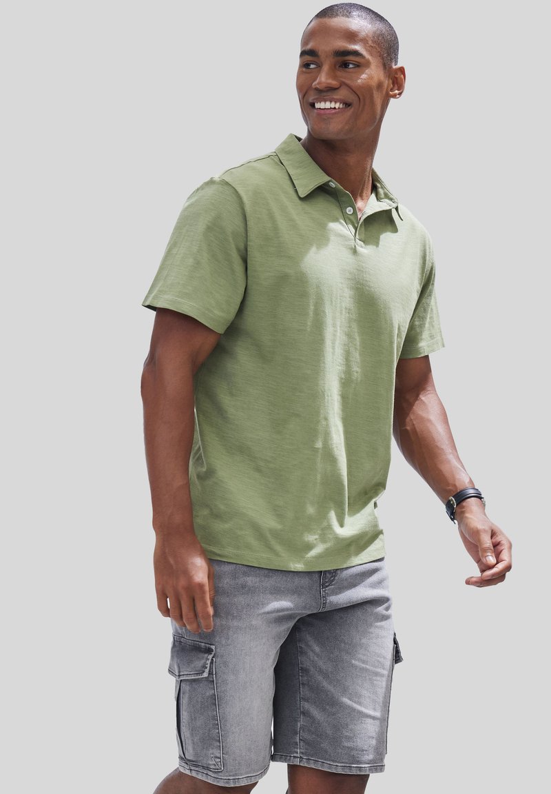 Hellgrünes Poloshirt mit Kragen, kurzen Ärmeln und lässiger Passform. Kombiniert mit grauen Cargo-Shorts mit Seitentaschen.