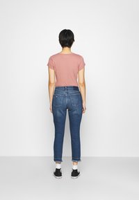 Vaaleanpunainen lyhythihainen t-paita yhdistettynä korkeavyötäröisiin, slim-fit sinisiin farkkuihin, joissa on röyhelöhelma, ja mustiin lenkkareihin, nähtynä takaa.