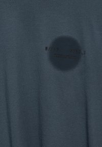 Mörkblå bomullströja med en cirkulär fläck och tryckt text med designkod och storleksmärkning på tyget, enhetlig struktur.