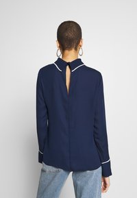 Granatowa koszula z długim rękawem, z białym wykończeniem kołnierza i szczegółem z otworem w tyle. Wykonana z gładkiego materiału, posiada mankiety zapinane na guziki.