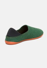 Pantofole verdi in feltro con un accento in tessuto nero sul retro e una suola in gomma arancione. Forma arrotondata con dettagli di cucitura puliti.