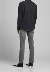 Camisa negra de manga larga, pantalones vaqueros ajustados grises y zapatillas altas negras con suelas blancas. Tela suave y diseño casual.