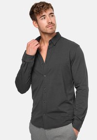 Camisa de botones de manga larga en gris oscuro, hecha de tela suave. Presenta un cuello clásico, puños con botones y un corte entallado.