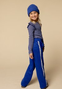 Blauw gestreepte lange mouwen top met ruches; blauwe wijde broek met hartpatroon witte zijstrips; blauwe gebreide muts; neutrale achtergrond.