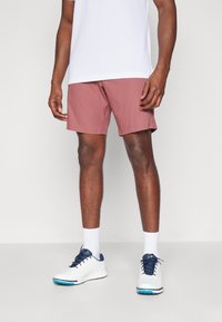 Korte rosa treningshorts med rett snitt, kombinert med hvite sokker og hvite joggesko med blå detaljer. En enkel hvit t-skjorte på toppen.