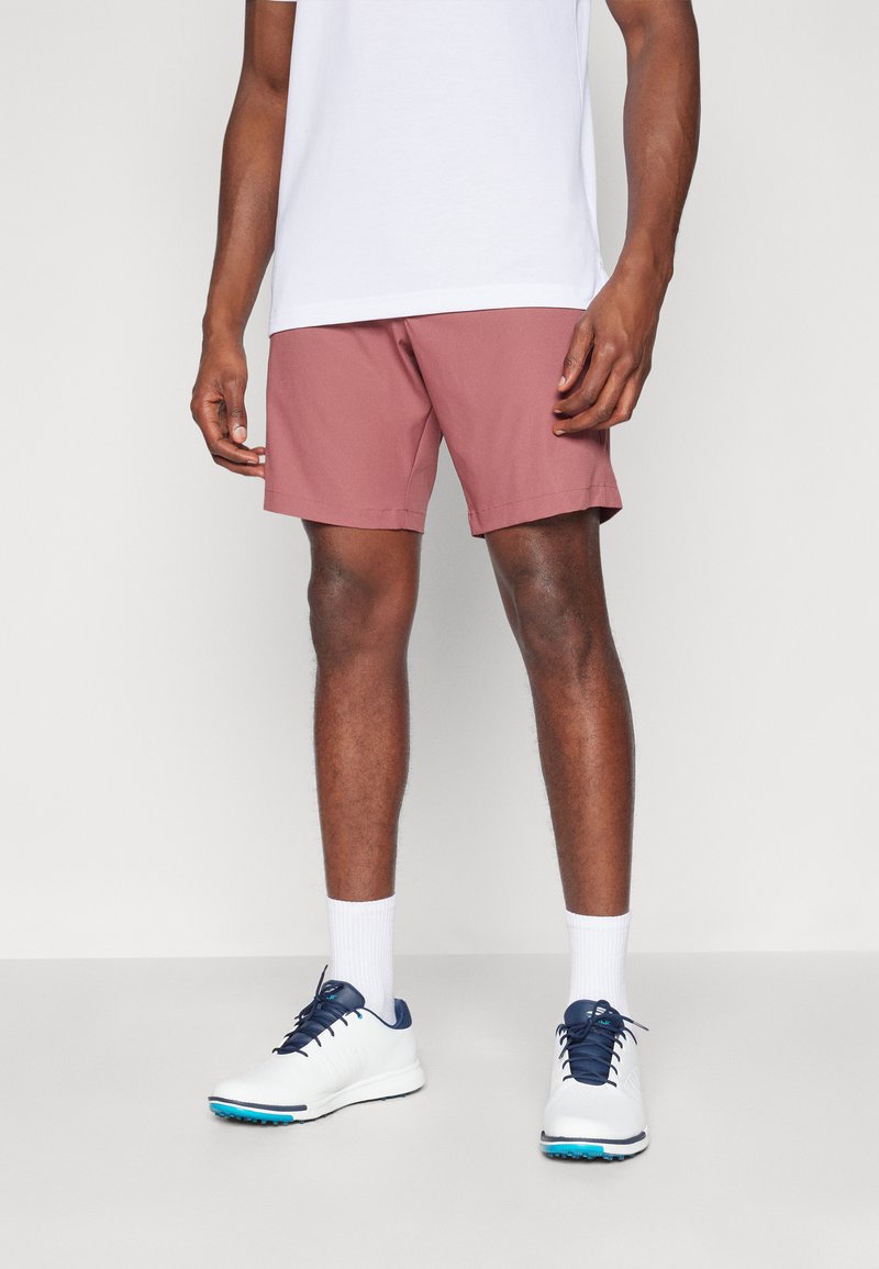 Korte rosa treningshorts med rett snitt, kombinert med hvite sokker og hvite joggesko med blå detaljer. En enkel hvit t-skjorte på toppen.