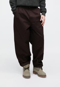 Pantalones holgados color burdeos oscuro con una textura suave, que cuentan con dos bolsillos delanteros y cierre de botón. Combinados con botas gris claro.