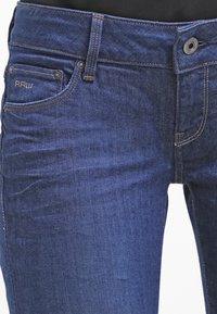 Vaqueros de mezclilla azul oscuro con corte recto, que presentan detalles de costura, una etiqueta de marca y un diseño estándar de cinco bolsillos.