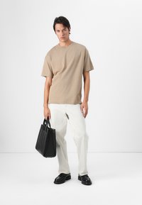 Beige kortærmet t-shirt, løstsiddende, parret med lyse, brede bukser. Sort læder tote bag og sorte sko, minimalistisk design.