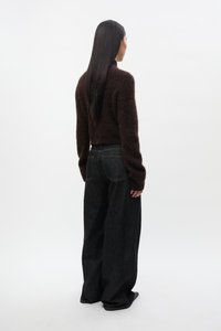 Pulover maro, pufos, cu mâneci lungi, asortat cu blugi evazați din denim închis la culoare, cu buzunare în spate și detalii subtile de cusături.