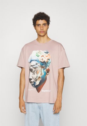 Lyserød bomulds T-shirt med grafisk tryk af et stiliseret ansigt med abstrakte elementer og teksten "forgotten fams." Løs pasform.