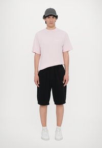 Pink short-sleeve t-shirt with a round neckline, black shorts with an elastic waistband, and white sneakers. Simple design, no patterns.