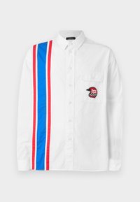 Hvid skjorte med knapper, der har et blåt og rødt stribedesign på den ene side og et sort broderet hjelm-patch på brystlommen.