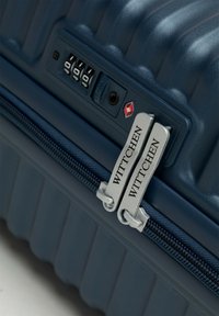 Maleta rígida azul con textura estriada, candado de combinación TSA y tiradores de cremallera metálicos etiquetados "WITTCHEN". Cremallera en un azul oscuro contrastante.