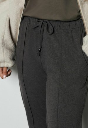 Pantaloni de trening gri închis cu talie elastică și detaliu cu șnur. Textură moale cu cusături laterale, asortați cu o jachetă fleece de culoare deschisă.