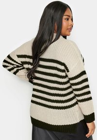 Stickad tröja med breda horisontella ränder i beige och mörkgrön, med en lös passform och ribbade ärmmuddar och nederkant. Texturerad garn ger djup.