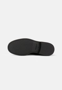 Suela de zapato negra con superficie de goma texturizada, forma redondeada y detalles de marca. Diseño contorneado para comodidad y agarre.