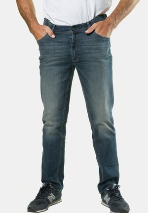 Jeans de mezclilla azul de corte ajustado con detalles desgastados, cinco bolsillos y cierre con cremallera. Combinados con zapatillas deportivas oscuras.