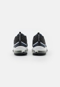Zapatillas deportivas en negro y marino con una parte superior texturizada, una media suela blanca y amortiguación de aire visible en el talón, con una trabilla en la parte trasera.