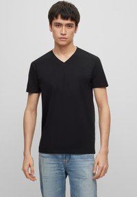 Black cotton V-neck t-shirt with short sleeves, fitted shape, and a smooth texture, paired with light blue denim jeans.