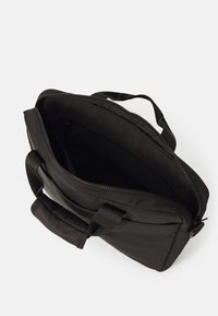Sort laptop taske af stof med en lynlås, to håndtag og en indvendig lomme. Indersiden er foret med et glat, blødt materiale.