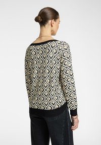 Suéter de punto con un patrón geométrico de diamantes en crema, negro y beige. Marga negra de canalé en el cuello y el dobladillo. Ajuste relajado.