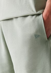 Ανοιχτό πράσινο παντελόνι jogger από απαλό, υφασμάτινο ύφασμα με υφή, με πλαϊνή τσέπη και μικρό ένθετο λογότυπο σε ταιριαστή απόχρωση.