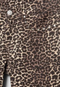 Taflă cu imprimeu de leopard, cu cuie metalice care conturează o buzunar frontal și un nasture metallic pe talia unui articol vestimentar.