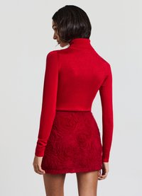Un pull col roulé rouge en tricot à manches longues associé à une mini-jupe rouge texturée avec un motif floral de roses. Fini lisse, design ajusté.