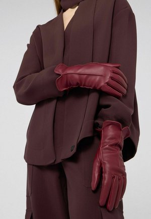 Weinrote Lederhandschuhe mit weicher Textur, tailliertem Design und dezenten gerafften Kanten, getragen von einem Model in einem passenden Outfit.