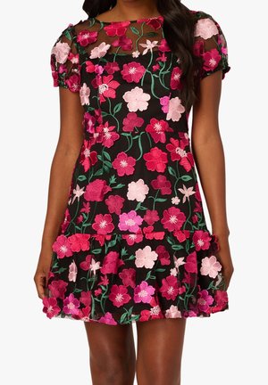 Femme portant une robe noire à manches courtes avec une broderie florale rose et rouge et un voile floral transparent par-dessus.