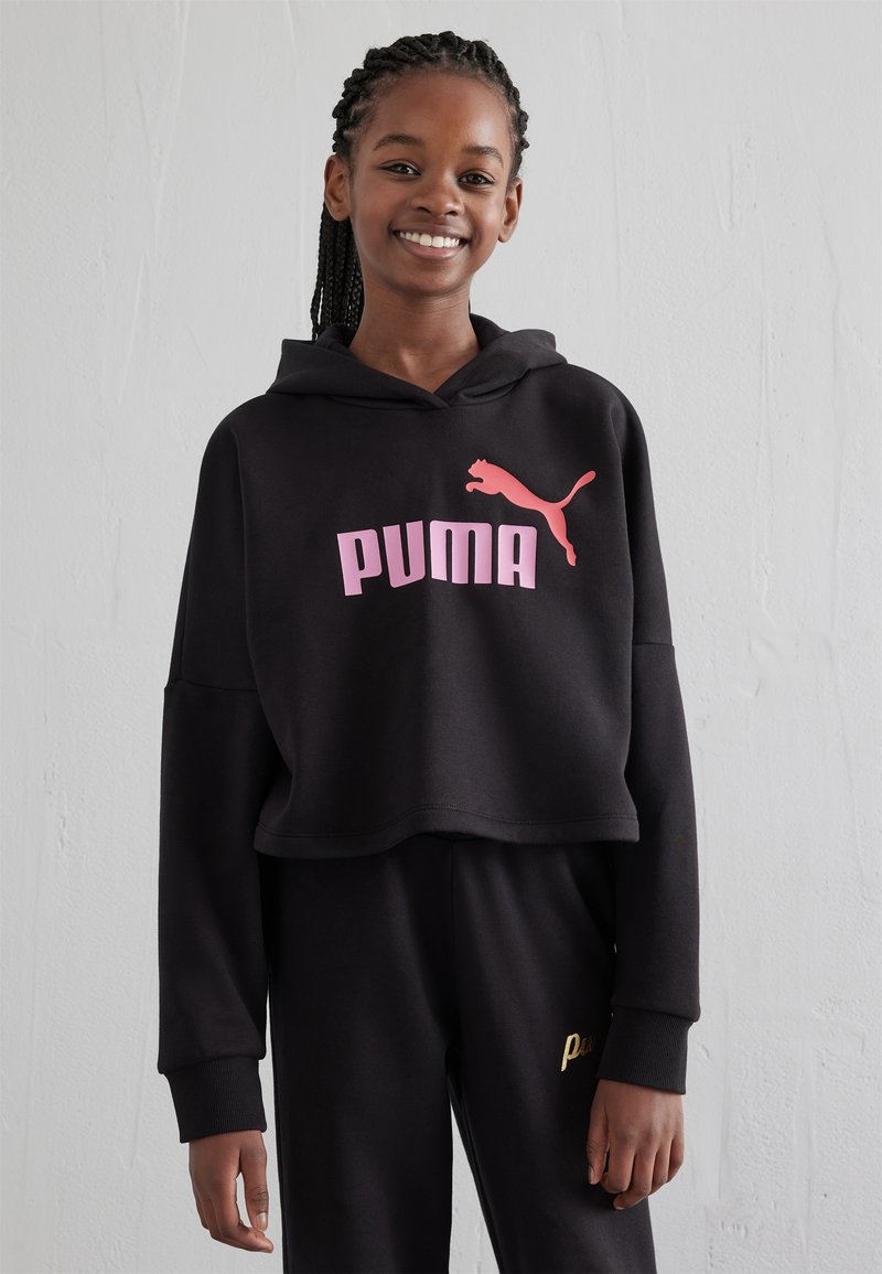 Sudadera corta negra de tejido suave, con un destacado logo de "PUMA" en rosa y una pequeña silueta de puma en rosa. Acompañada de pantalones negros.