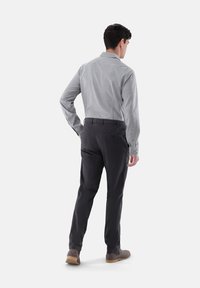 Schwarzes und weißes kariziertes Langarmhemd in taillierter Passform, kombiniert mit dunklen Hosen und hellbraunen Stiefeln, von hinten betrachtet.