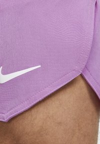 Lila idrottsshorts med en vit Nike-logotyp, som bärs på en persons lår där lite hår syns.