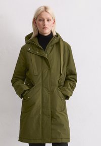 Olivgrön parkas tillverkad av vattenavvisande material, med huva, dragkedjestängning, sidofickor och vadderad design för värme.
