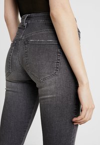 Jeans de mezclilla gris de cintura alta con dos bolsillos traseros, un ligero desvanecimiento y una silueta ajustada, que exhiben una textura suave.