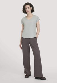 Lichtgroen v-hals t-shirt met opgerolde mouwen, gecombineerd met ruime donkerbruine broek en zwarte schoenen met franjes.