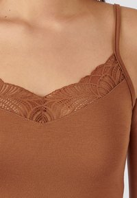 Brown tank top with lace trim along the neckline, featuring a smooth, ribbed texture and thin adjustable straps.