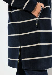 Cappotto in pile navy con strisce bianche, tasca con zip e spacco laterale con un accento giallo all'orlo. Tessuto morbido e vestibilità comoda.