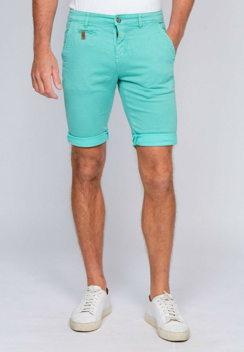 Shorts en coton vert menthe avec des revers, poches avant et une poche arrière. Comprend une fermeture à bouton et à zip.