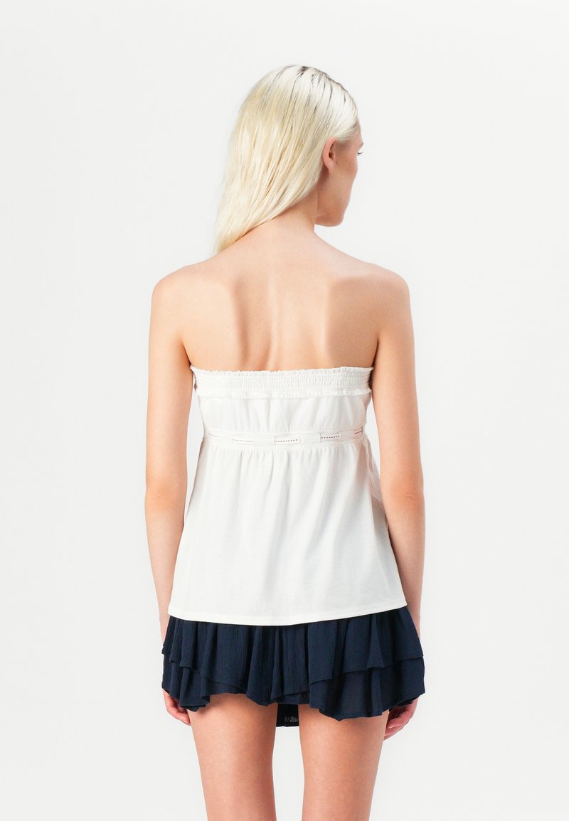 Weißes trägerloses Oberteil mit gerafftem Bund, kombiniert mit einem dunkelblauen Rüschenrock mit Schichten. Schlichte Linien, weicher Stoff und eine fließende Silhouette.