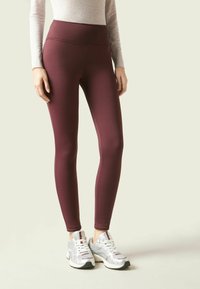 Leggings granate en un diseño ajustado, hechos de una tela suave con una cinturilla alta. Combinados con zapatillas deportivas plateadas y blancas.
