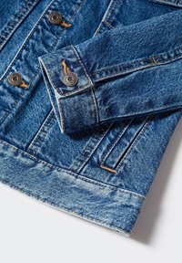 Džínová bunda, modrá tkanina, manžety na knoflíky, dvě přední kapsy, světlé prošívání, drsná textura, s mírně roztrhaným lemem.