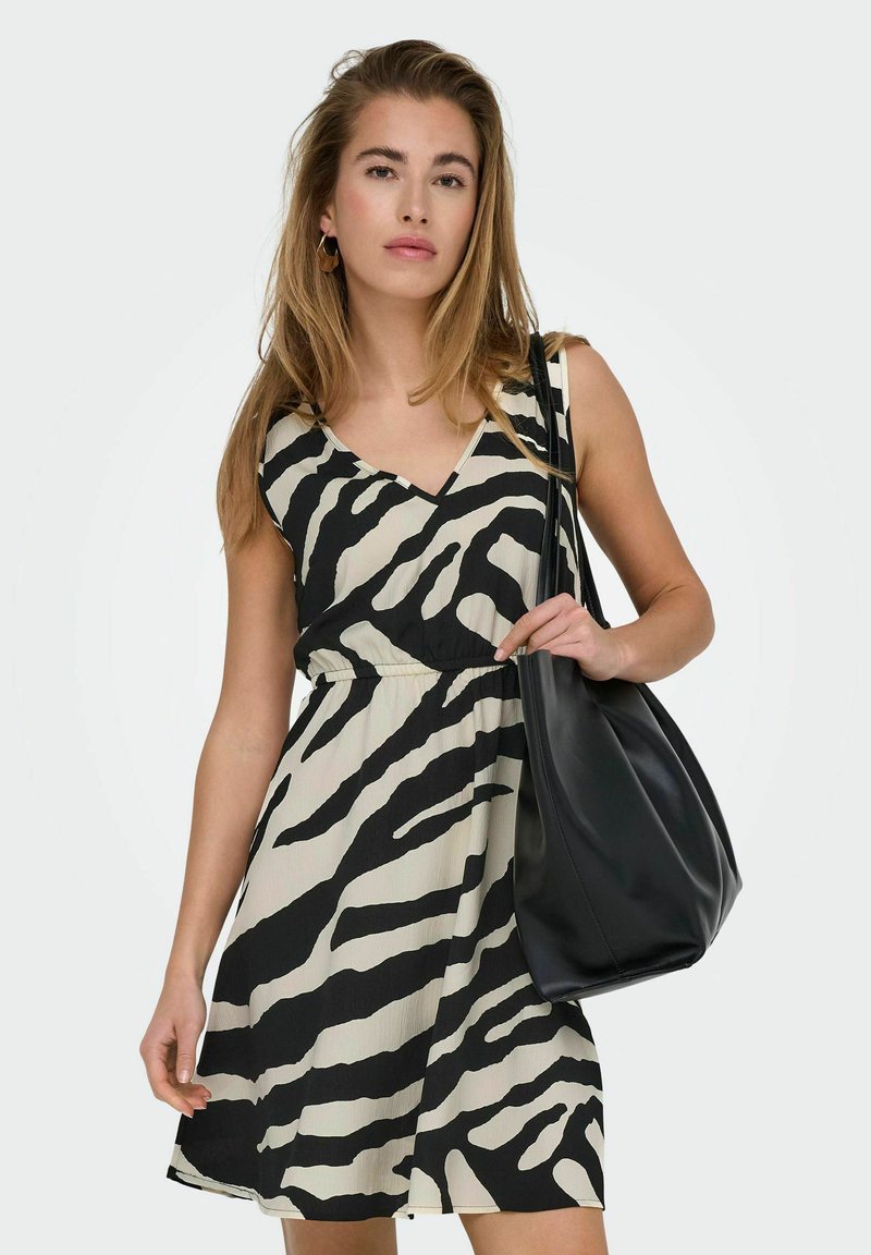 Vestido de rayas de cebra en negro y beige con escote en V y cintura elástica, acompañado de un bolso de hombro de cuero negro.